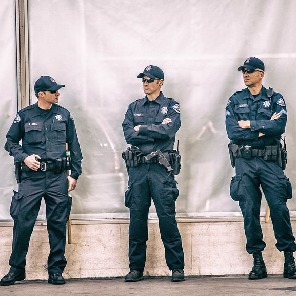 A group of uniformed police officers stand together on the sidewalk.