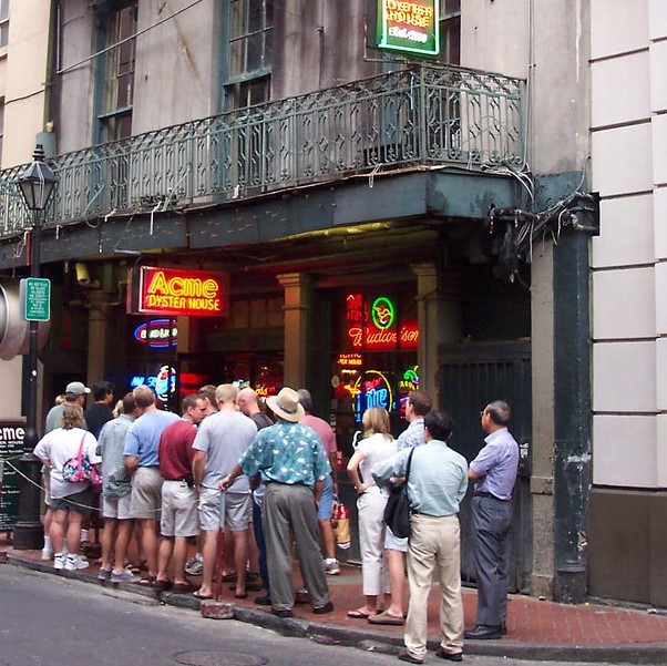 Una larga fila de personas se paran en la acera frente a un restaurante esperando para entrar.