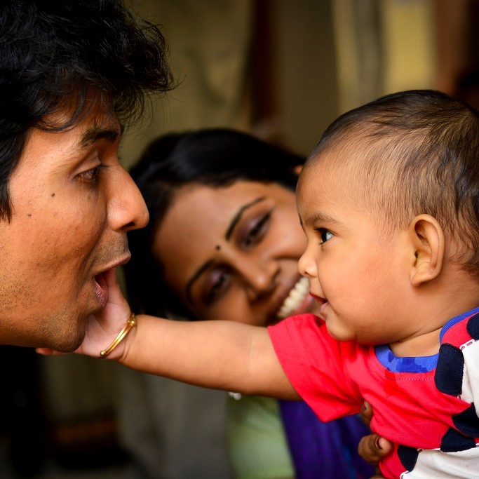 Un bebé se acerca para tocar la cara de su padre sonriente mientras mira una madre feliz.