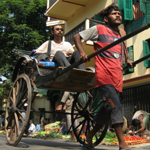 Un conductor de rickshaw tira a un pasajero por una calle de la ciudad.