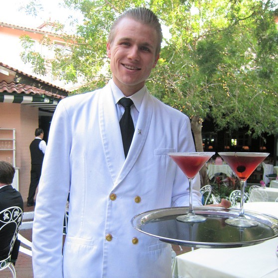 Un mesero sonriente entregando cócteles en una bandeja.