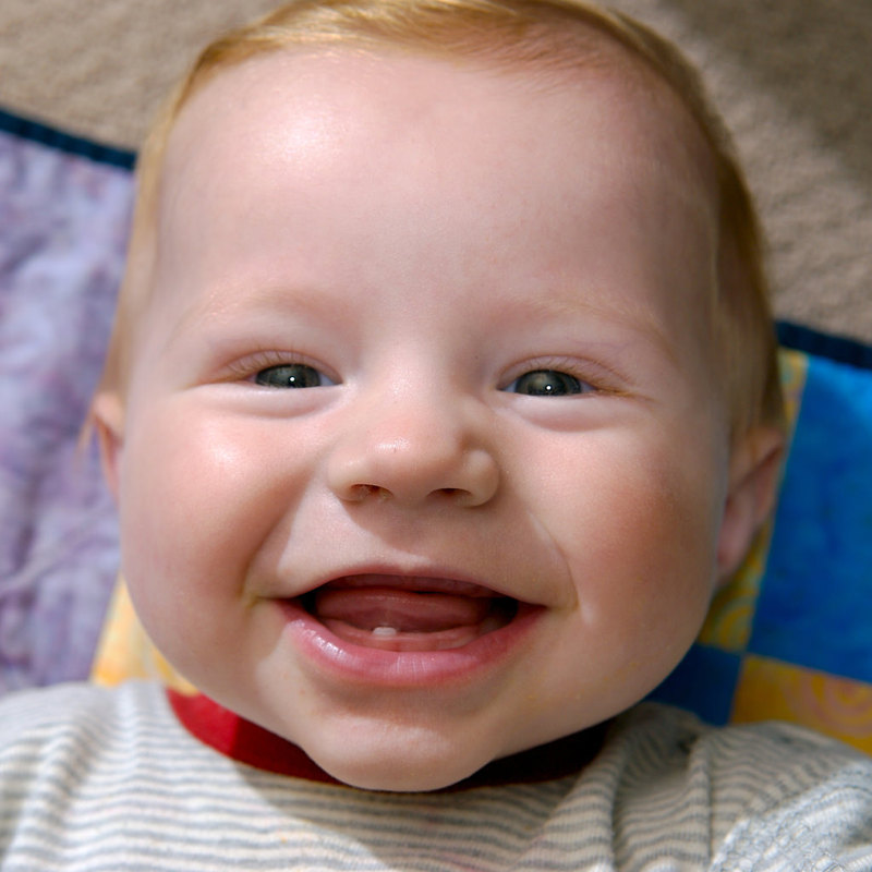 A baby smiling and showing his first tooth.
