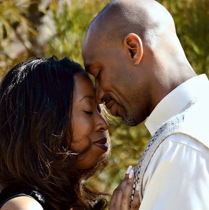 A man and woman in a tender embrace smile with eyes closed.