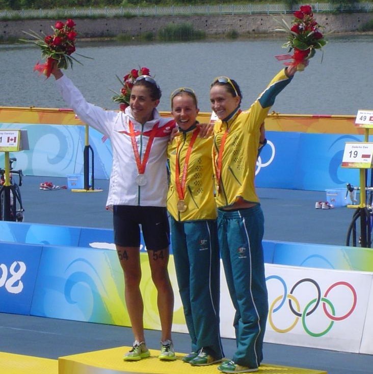 Trzy medalistki w triathlonie olimpijskim kobiet w 2008 roku stoją razem na podium zwycięzców.'s Olympic Triathlon stand together on the winner's podium.