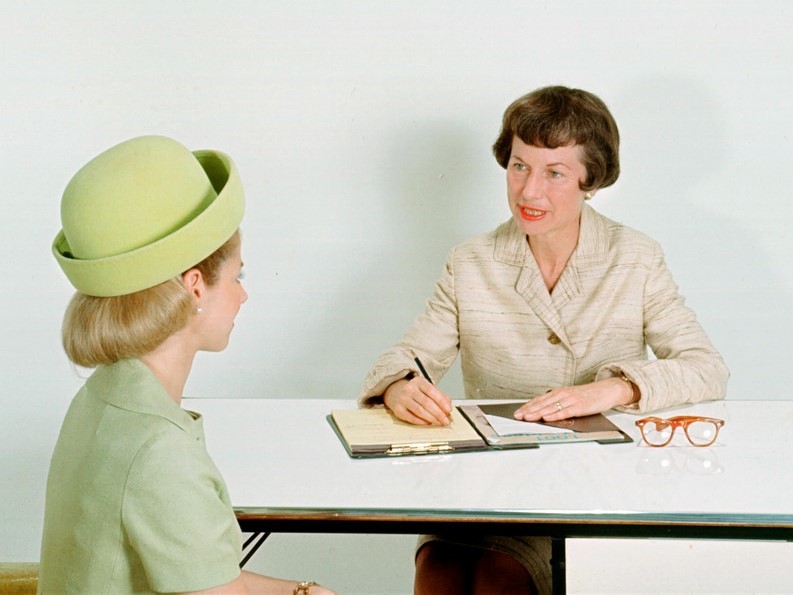 Dos mujeres se sientan frente a una mesa una de otra durante una entrevista de trabajo.