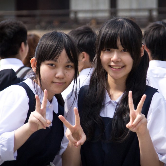 Dos colegialas japonesas sonríen y muestran un típico “signo V” como pose para una foto.