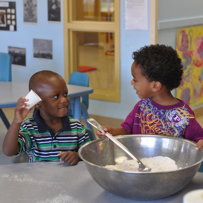 Two young boys happily cooperating on putting the ingredients together for a recipe.