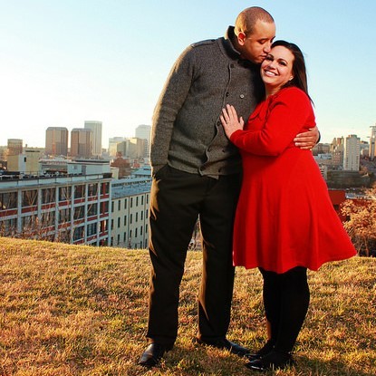 A young, attractive couple pose for a photo in front of a city skyline.