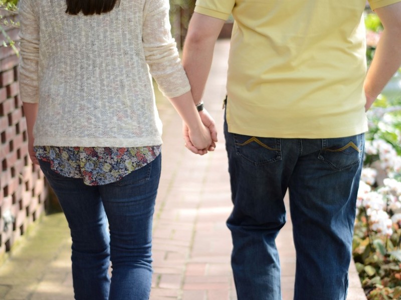 Una pareja cogidos de la mano mientras caminan por la acera.