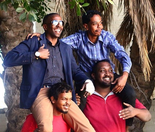 A happy group of young men pose for a photo. Two of them sit smiling on the shoulders of their friends below.