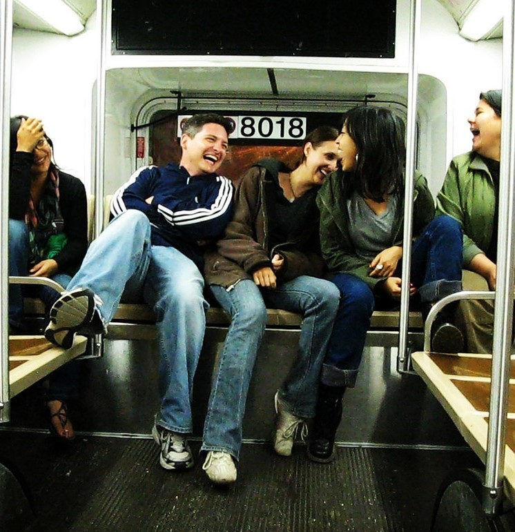 A group of friends sit in the back of a bus laughing together.