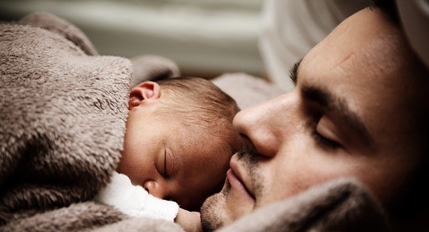 A father sleeps with an infant asleep on his chest.