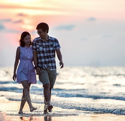 A young couple walk down the beach at sunset hand in hand.