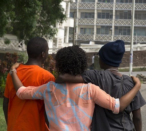 Three friends walk down the street with their arms over one another's shoulders.