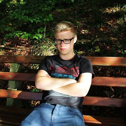 A dejected looking young man sits alone with arms crossed on a park bench.