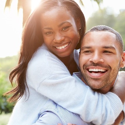 A man holds his partner on his back as she embraces him around the neck.