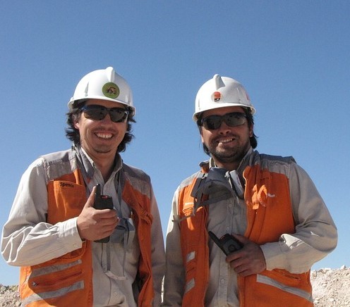 Dos ingenieros mineros vestidos con equipo de seguridad sonriendo juntos en un sitio de trabajo.