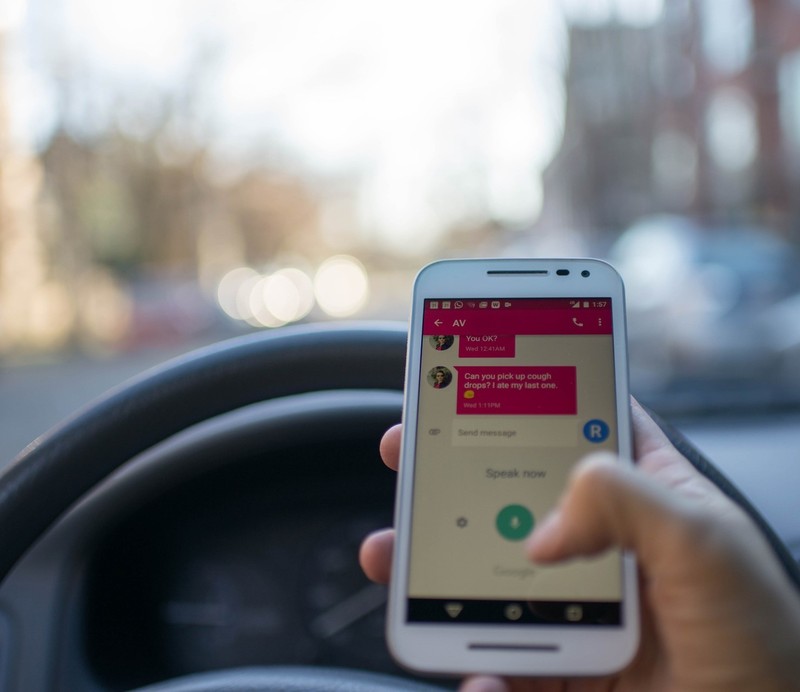 Image shows the point of view of a driver as she texts while behind the wheel.