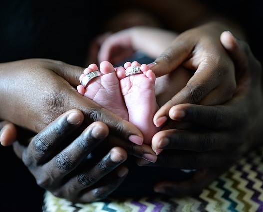 The hands of a mother and father cupping the tiny feet of a very small baby.