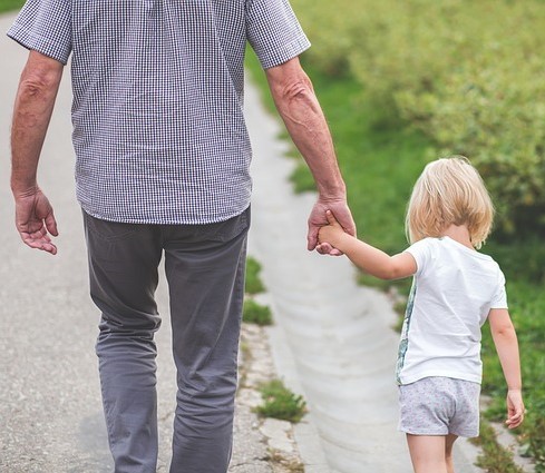 A father and his small daughter walk along the road holding hands.