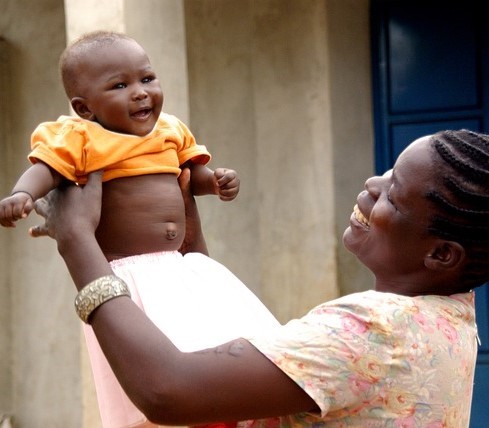 A mother playfully lifts her baby above her head to the bay's delight.