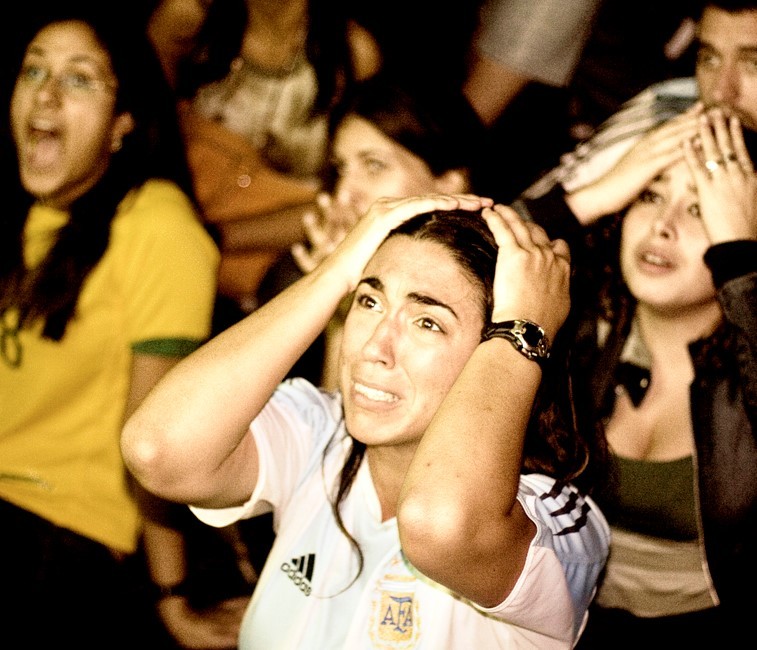 An Argentine soccer fan wearing a national team jersey reacts in horror as she watches a match on television.