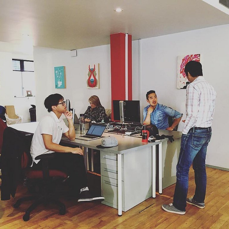 A group of office workers gather around a desk during a conversation.