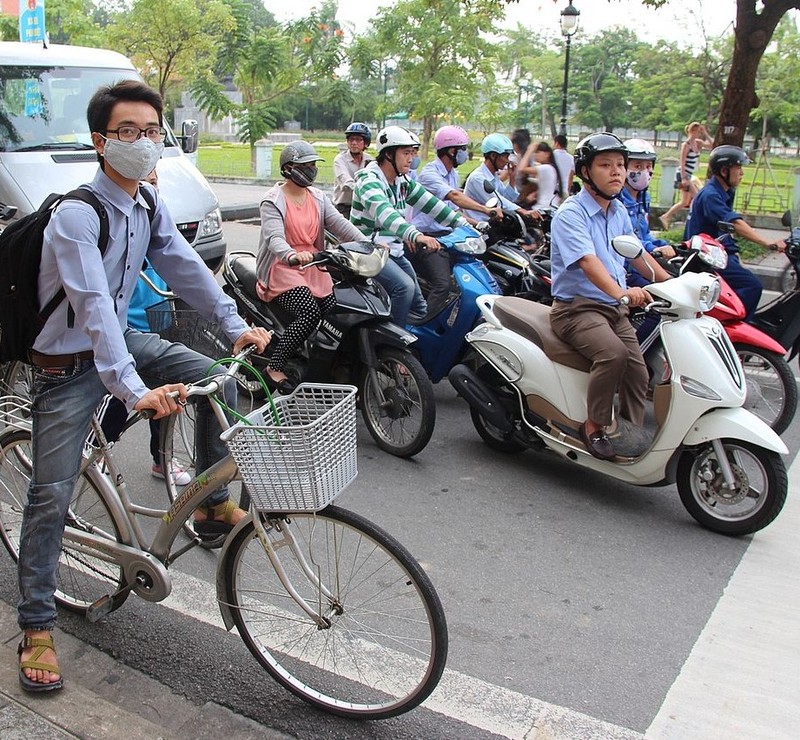 A group of motor scooters and a bicyclist wait at an intersection for the traffic light to change.