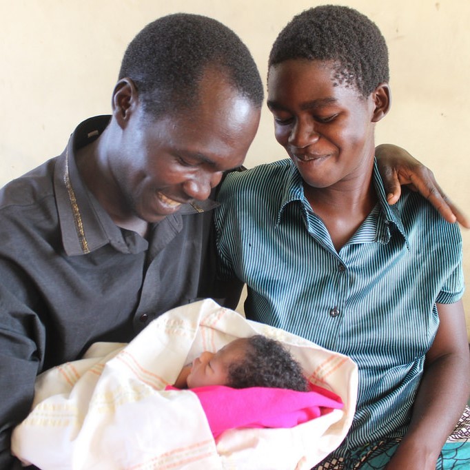 Una joven madre y un padre son todos sonrisas mientras sostienen a su bebé.