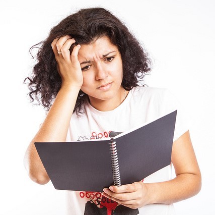 A student looks with confusion into a notebook.