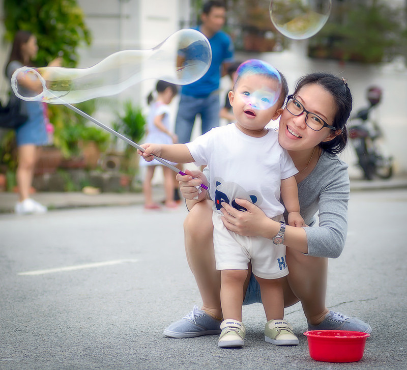 A mother helps her young son use a bubble wand.
