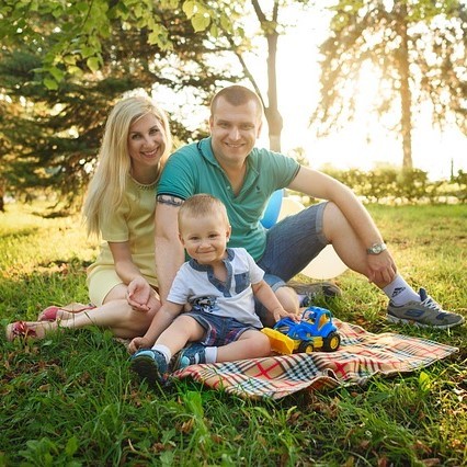 A young mother and father sit with their toddler son on the lawn.