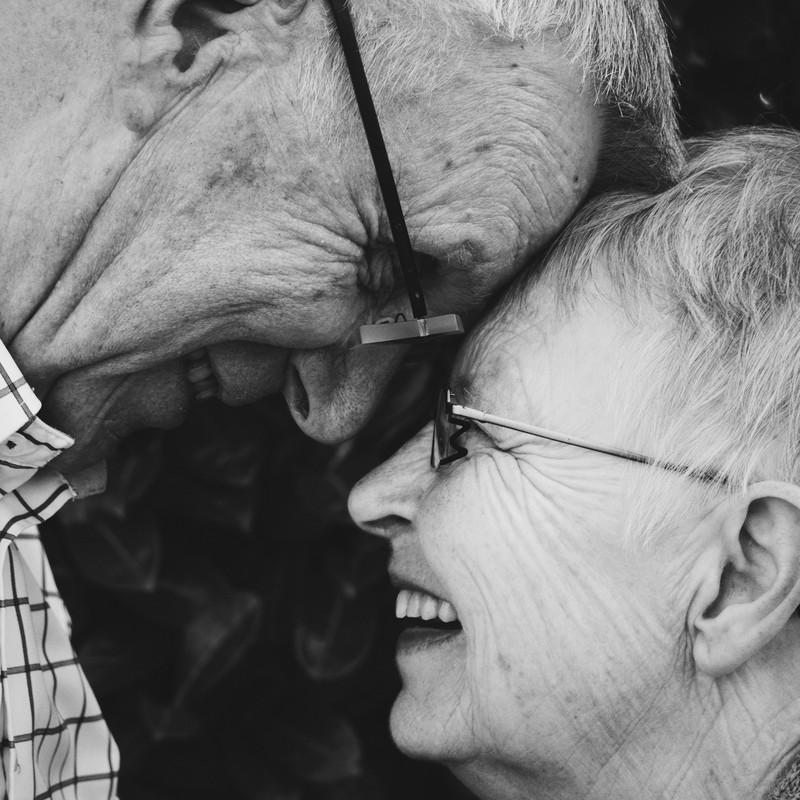 An elderly couple embrace and look into each other's eyes.