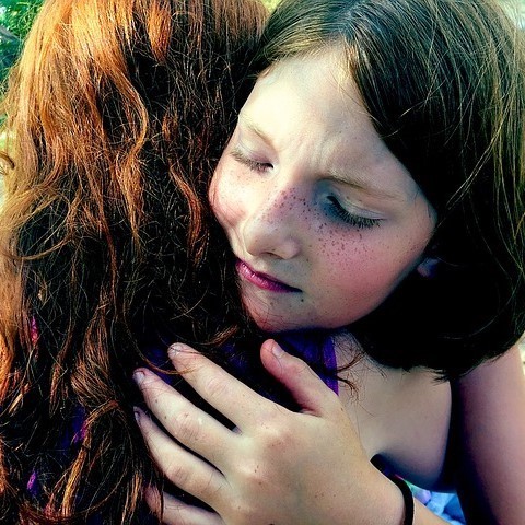A girl closes her eyes as she hugs her friend.