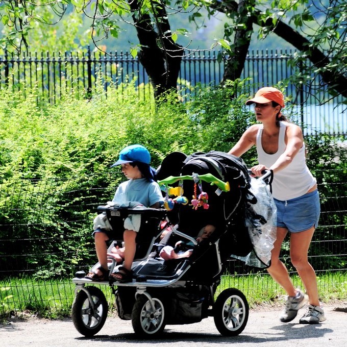 Una mujer corre por un parque con tres niños pequeños en una carriola.