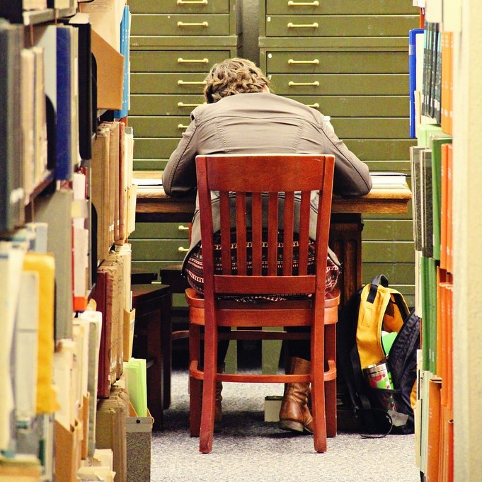 Un estudiante está encorvado sobre un escritorio en la biblioteca.