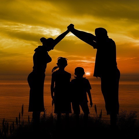 A mother and father standing on either side of their children and join hands as a symbolic roof over their heads.