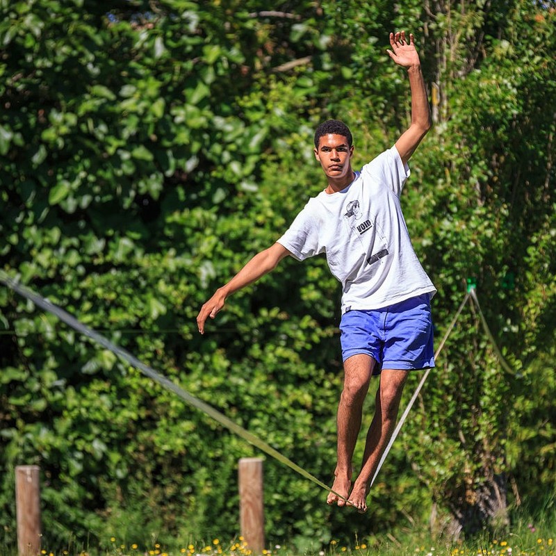 Un hombre camina a través de un slackline con los brazos extendidos para lograr el equilibrio.