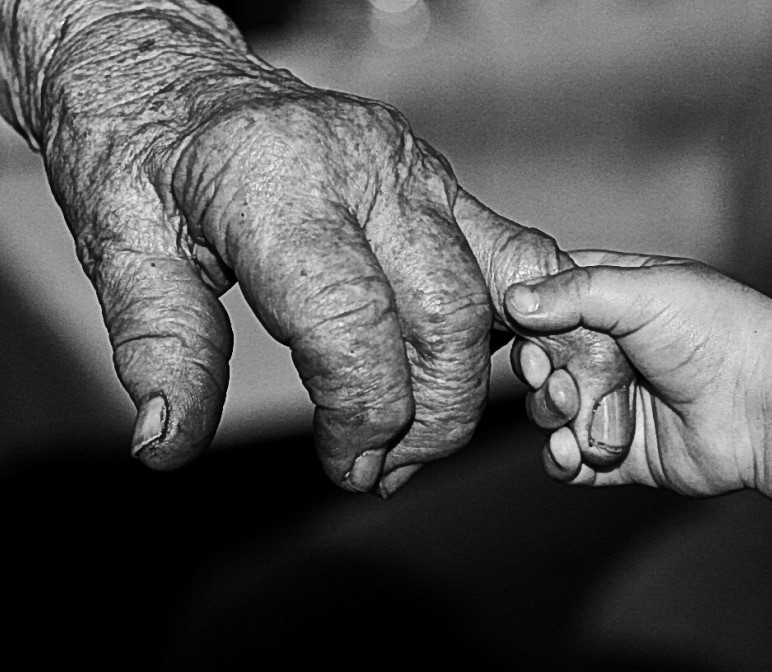 Una mano muy pequeña de un niño sostiene un dedo arrugado en la mano de una persona muy mayor.