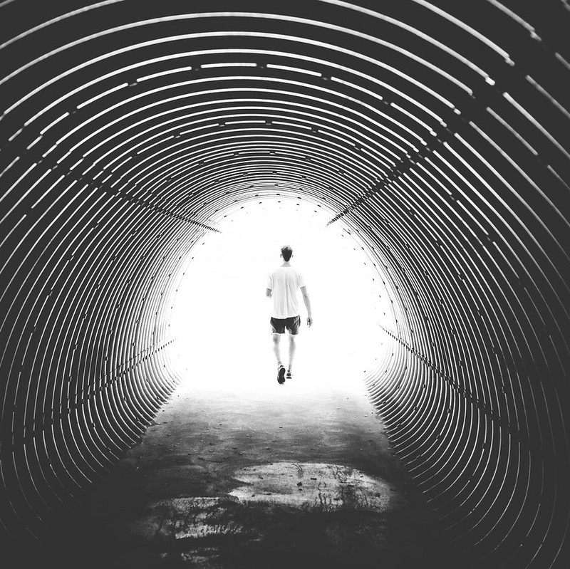A man walks out of a dark tunnel into bright daylight.