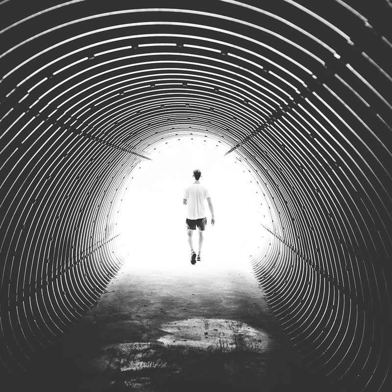 Un hombre sale de un túnel oscuro hacia la luz del día brillante.