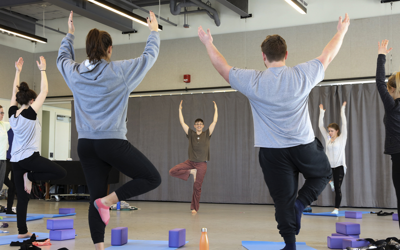 A yoga instructor and a group of students practicing tree pose.