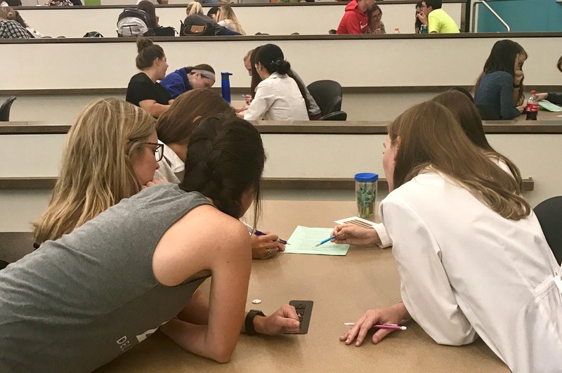 A group of students arranged around a table are working together to solve a problem.