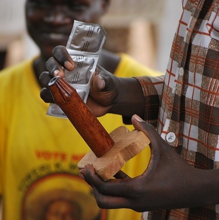 A sex education instructor holds a package of condoms and a wooden model of a penis before giving a demonstration of proper condom use.