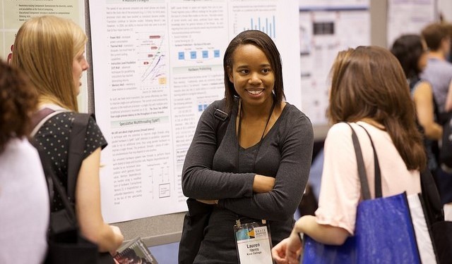 Students at a conference gathered around a poster presentation. 