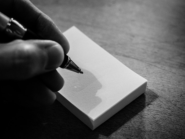 A hand writing on a note card with a pen.