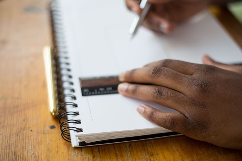 A person using a ruler and pen in a notebook