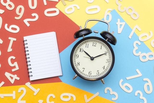 An image depicting deadlines: An alarm clock, a notebook and various numbers lying around it