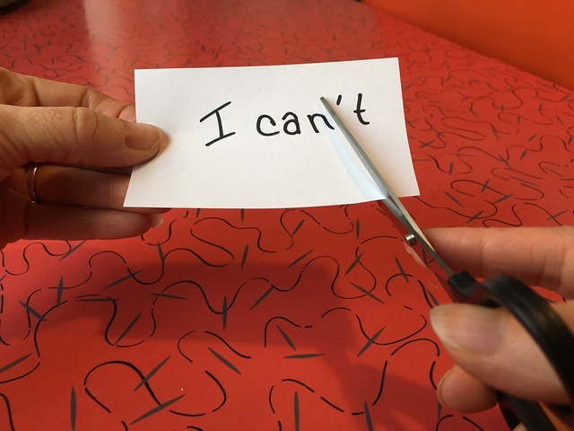 A hand holing a piece of paper with the words "I can't" written on it and a pair of scissors in the other hand cutting the piece of paper.