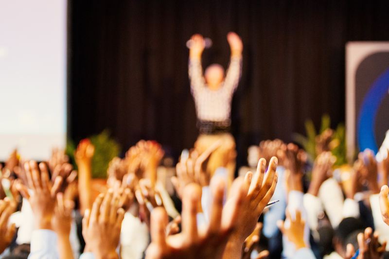 A zoomed out image of a speaker on stage and the audience